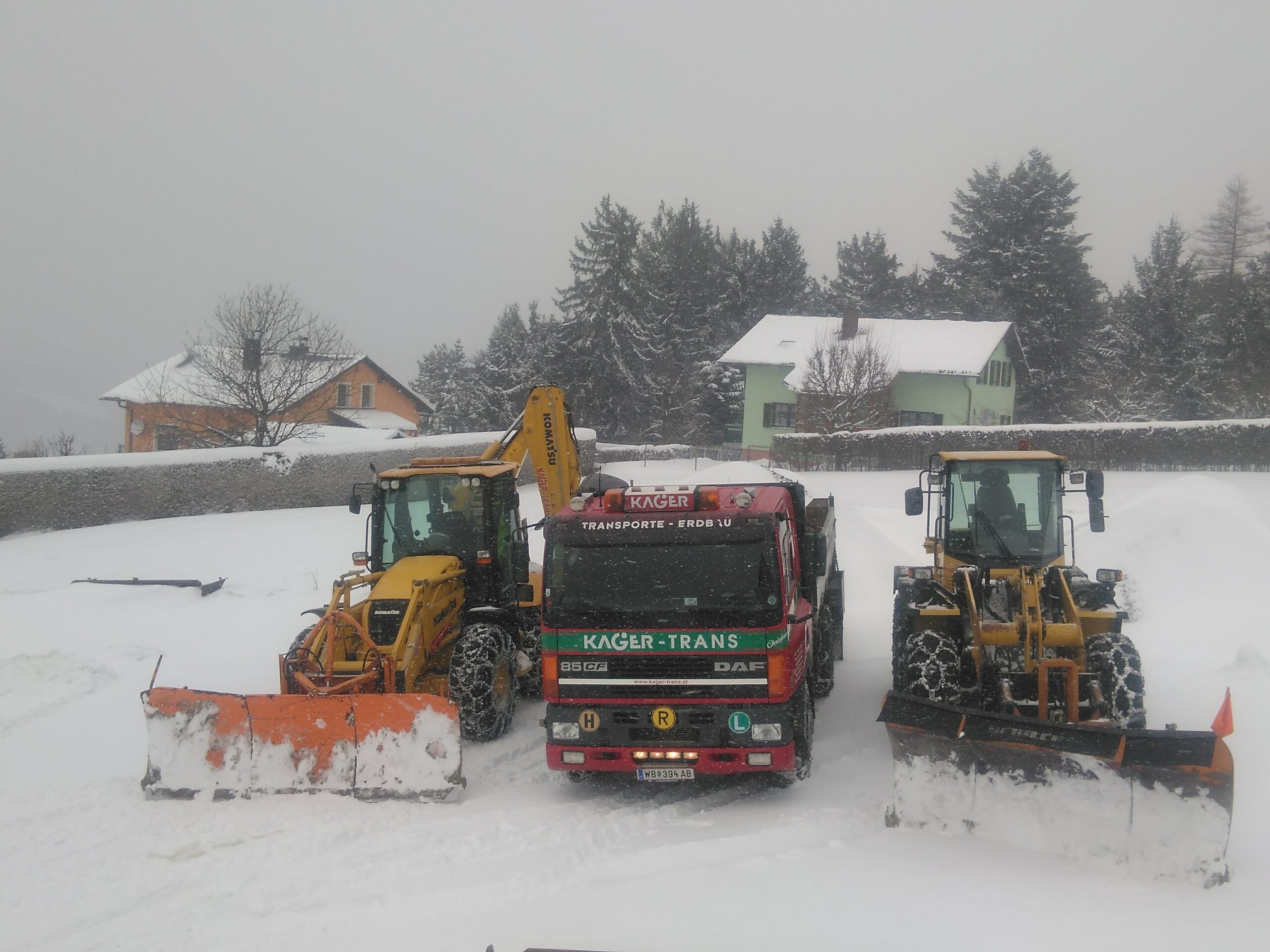 Ein roter Lkw mit zwei gelben Baggern mit Schneepflügen im Schnee. 