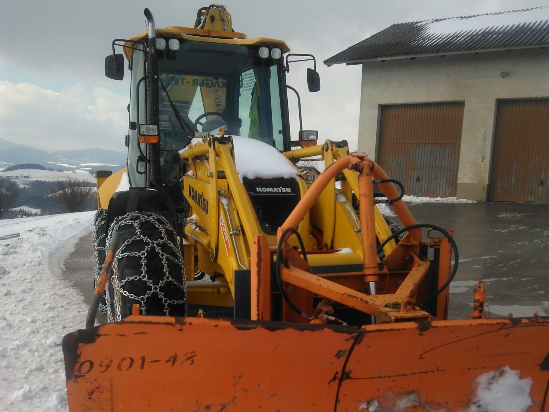 Komatsu-Radlader mit Schneepflug räumt Schnee auf einer Zufahrt.