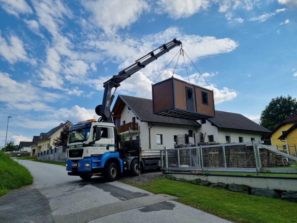 LKW mit Kran hebt ein vorgefertigtes Modulhaus auf ein Fundament