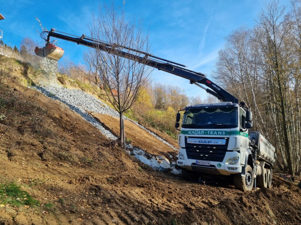 Kran-LKW verteilt Schotter zur Hangsicherung in steilem Gelände